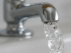 A close-up of a chrome tap with clear water flowing from the spout into a white basin.