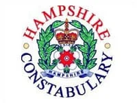 Logo of Hampshire Constabulary, featuring a crown, a red and white rose, and green laurel wreath, with the words Hampshire Constabulary in red and blue around the emblem.