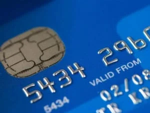 Close-up of a blue credit card showing the chip and part of the card number, with raised silver digits and VALID FROM information visible.