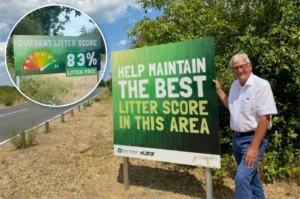 A man stands next to a sign that says, Help maintain the best litter score in this area. An inset shows a gauge indicating an 83% litter-free score. Both signs are by a roadside with greenery.